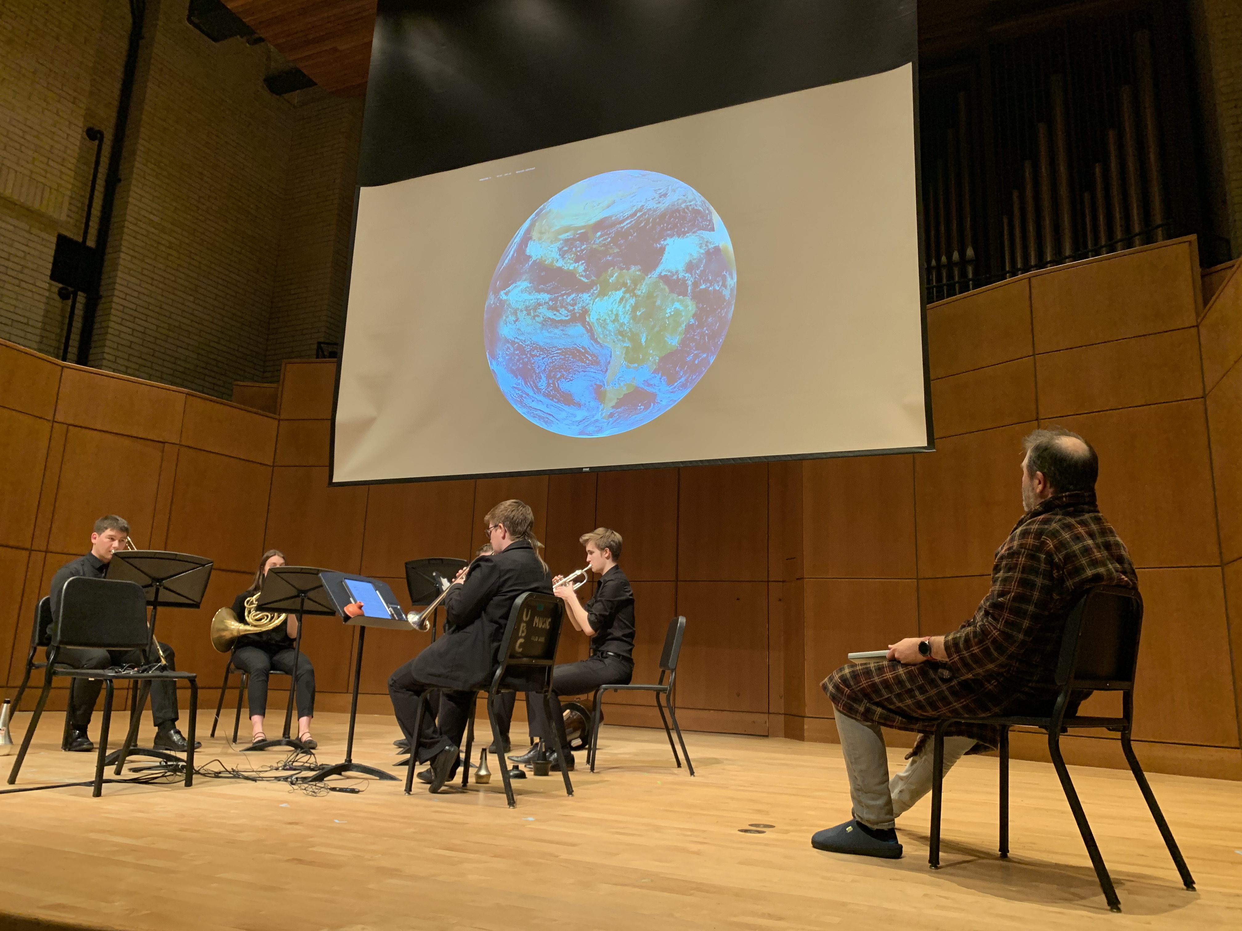 A brass quintet playing music on a stage with an image of Earth projected on a screen behind them.