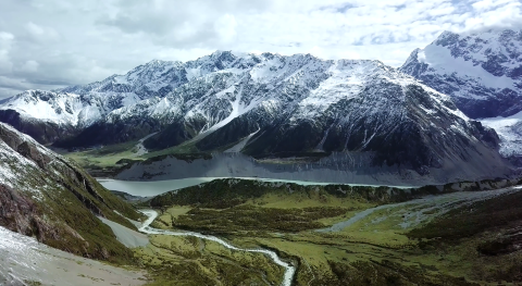 A snow capped mountain range above a green glacially carved valley.